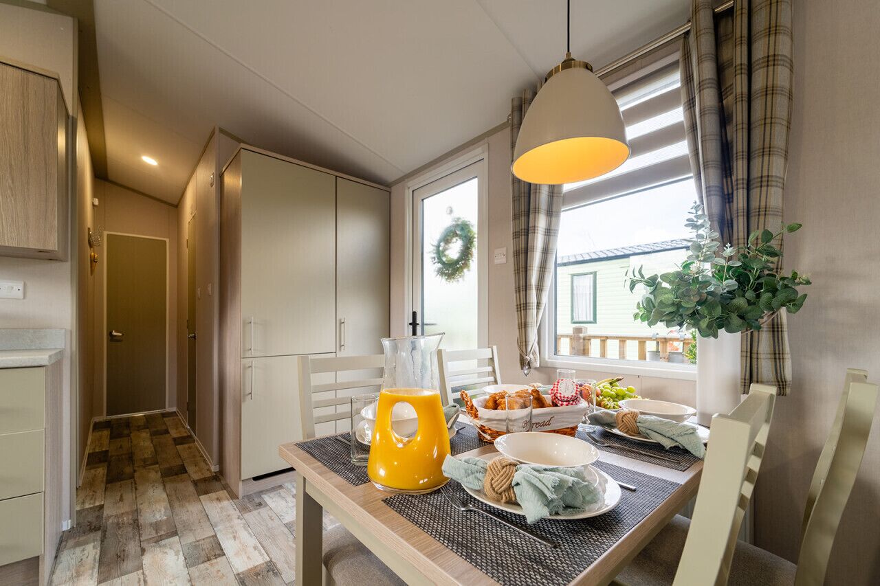 Un comedor con una mesa lista para el desayuno, que incluye una jarra de jugo de naranja, una cesta de pan y un bol de fruta.