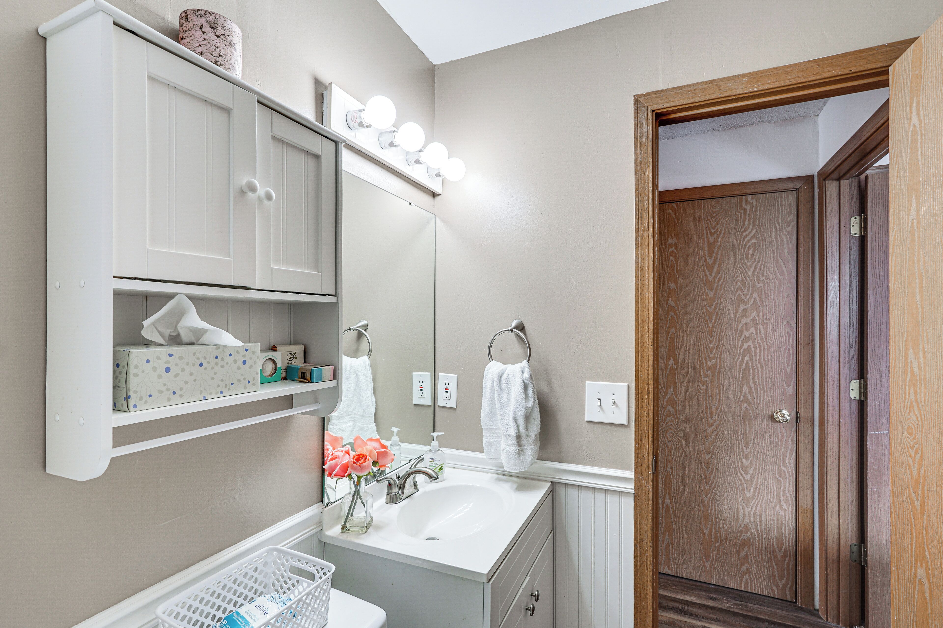 A bathroom with a vanity, mirror, sink, and a wooden door.