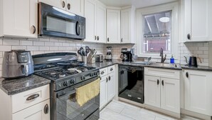 Een moderne keuken met witte kasten, een roestvrijstalen fornuis, een magnetron en een vaatwasser.