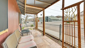 A covered porch with a bench and a table, a wooden fence, and a view of a street and buildings in the background. - Downtown Williams Home: Walk to Shops & Dining! (Williams)