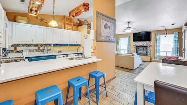 A modern kitchen with white cabinets, a central island with stools, and a dining area with a white table and chairs. - Downtown Williams Home: Walk to Shops & Dining! (Williams)