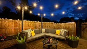 A wooden deck with a sofa and a fire pit, surrounded by a wooden fence and string lights. - Pet & Family Friendly! Home w/ Fenced Yard + Deck (York Haven)