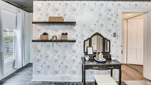 A hallway with a floral wallpaper, a dark wooden console table with a mirror, shelves with baskets, and a bench. - Pet & Family Friendly! Home w/ Fenced Yard + Deck (York Haven)