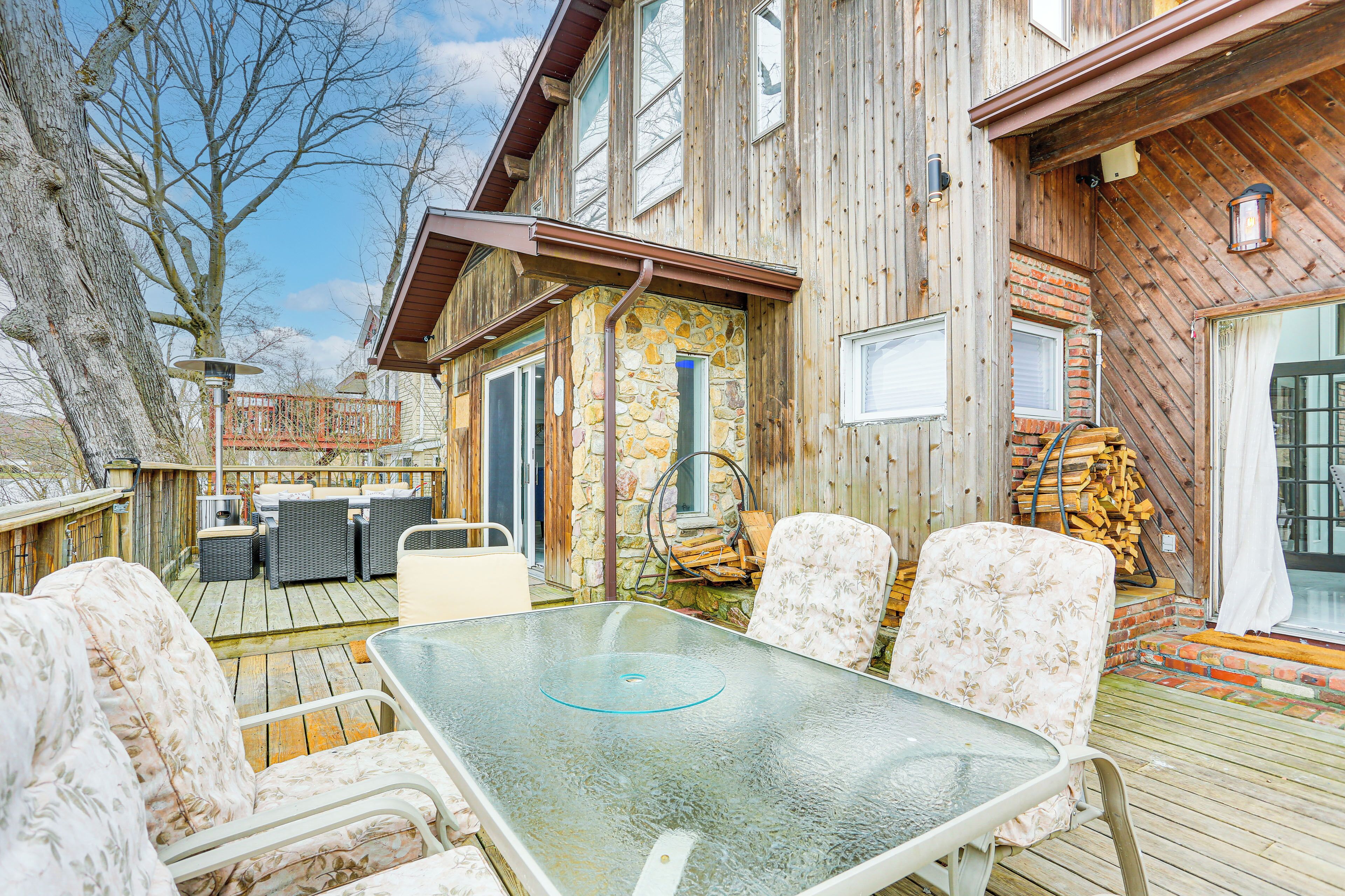 A wooden deck with a glass table and chairs, a stone wall, and a wooden staircase.