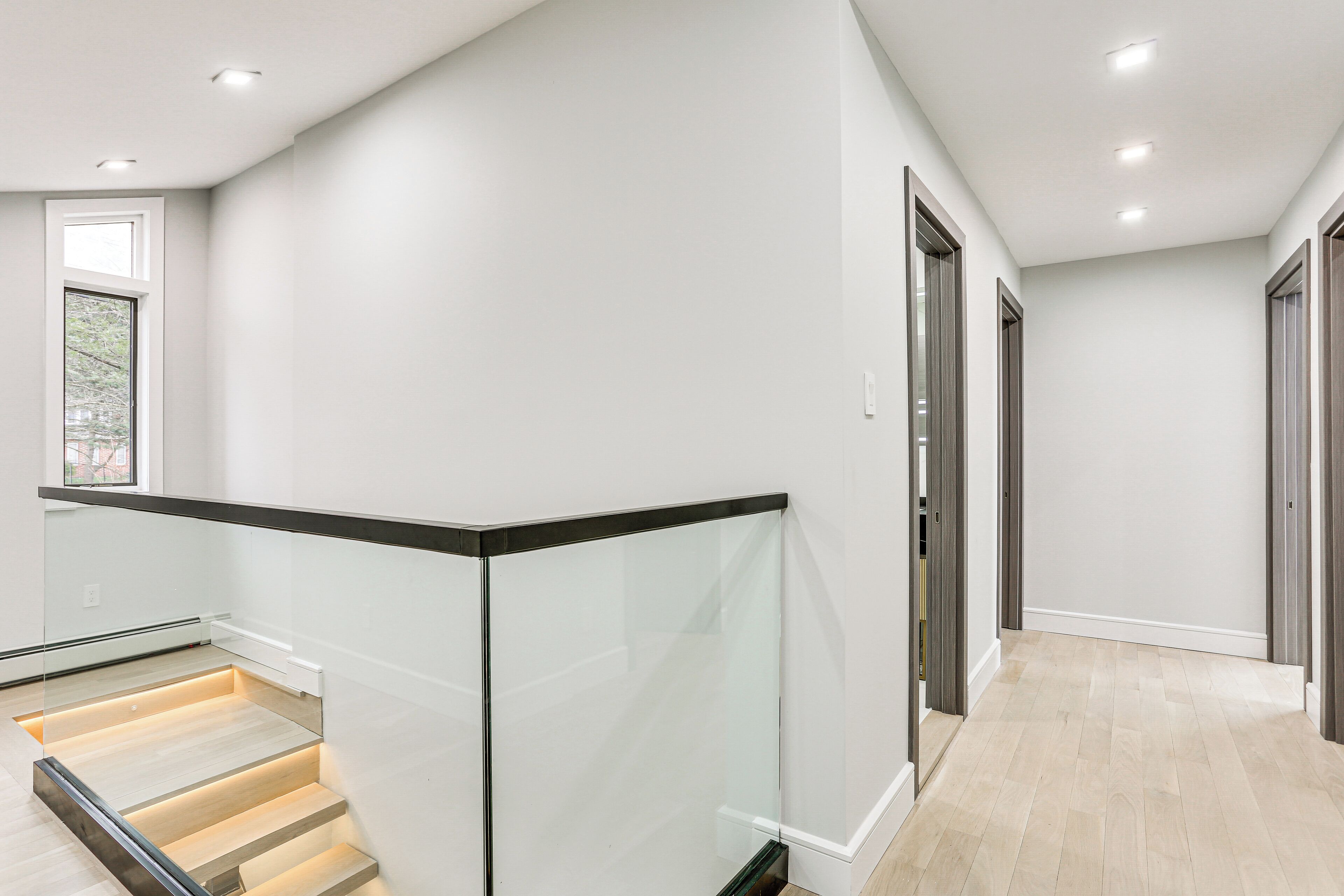 Een modern interieur met een glazen balustrade, een hal met houten vloer en een deur met donker frame.