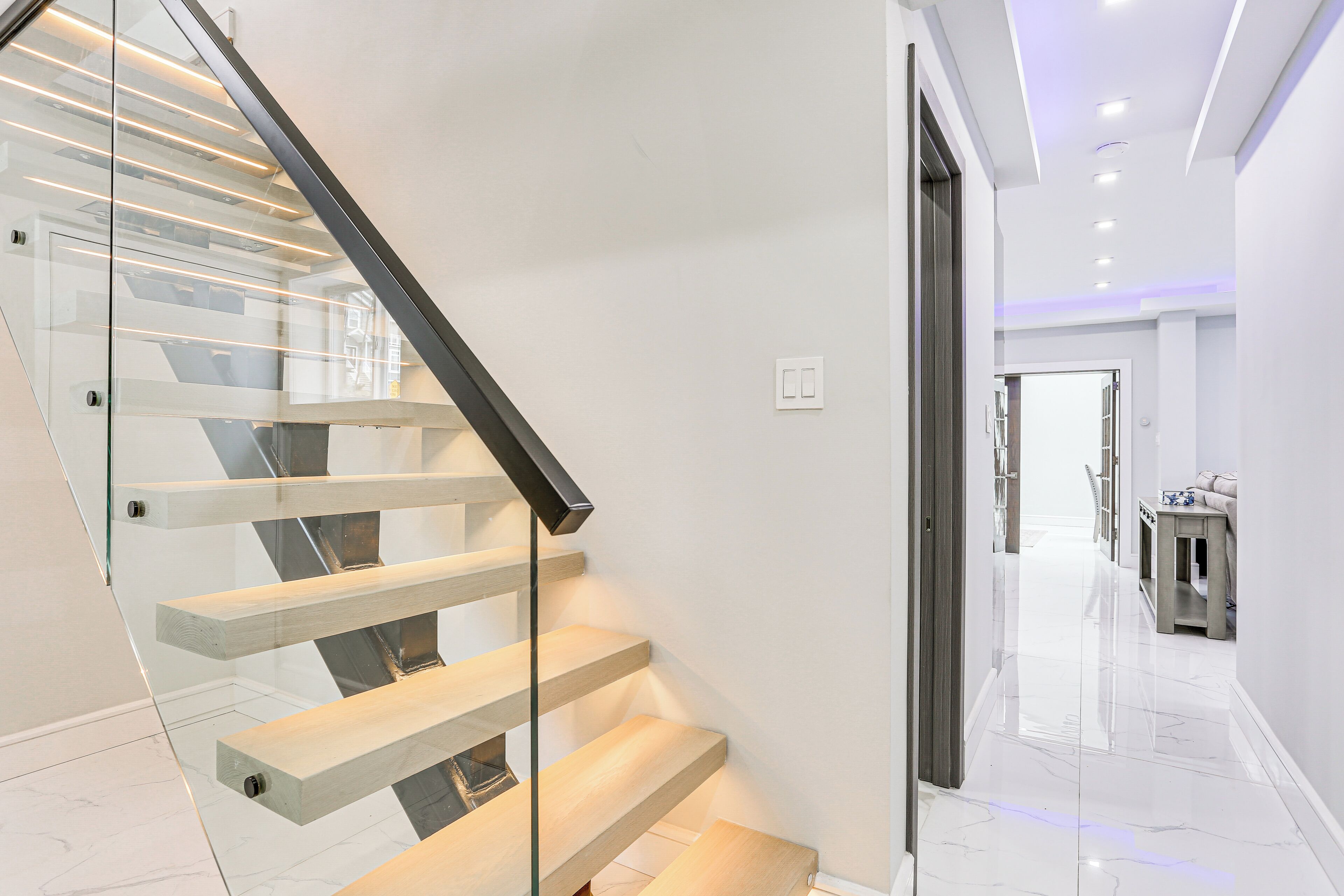 Una escalera moderna con barandillas de vidrio y escalones de madera, que conduce a un espacio interior bien iluminado.