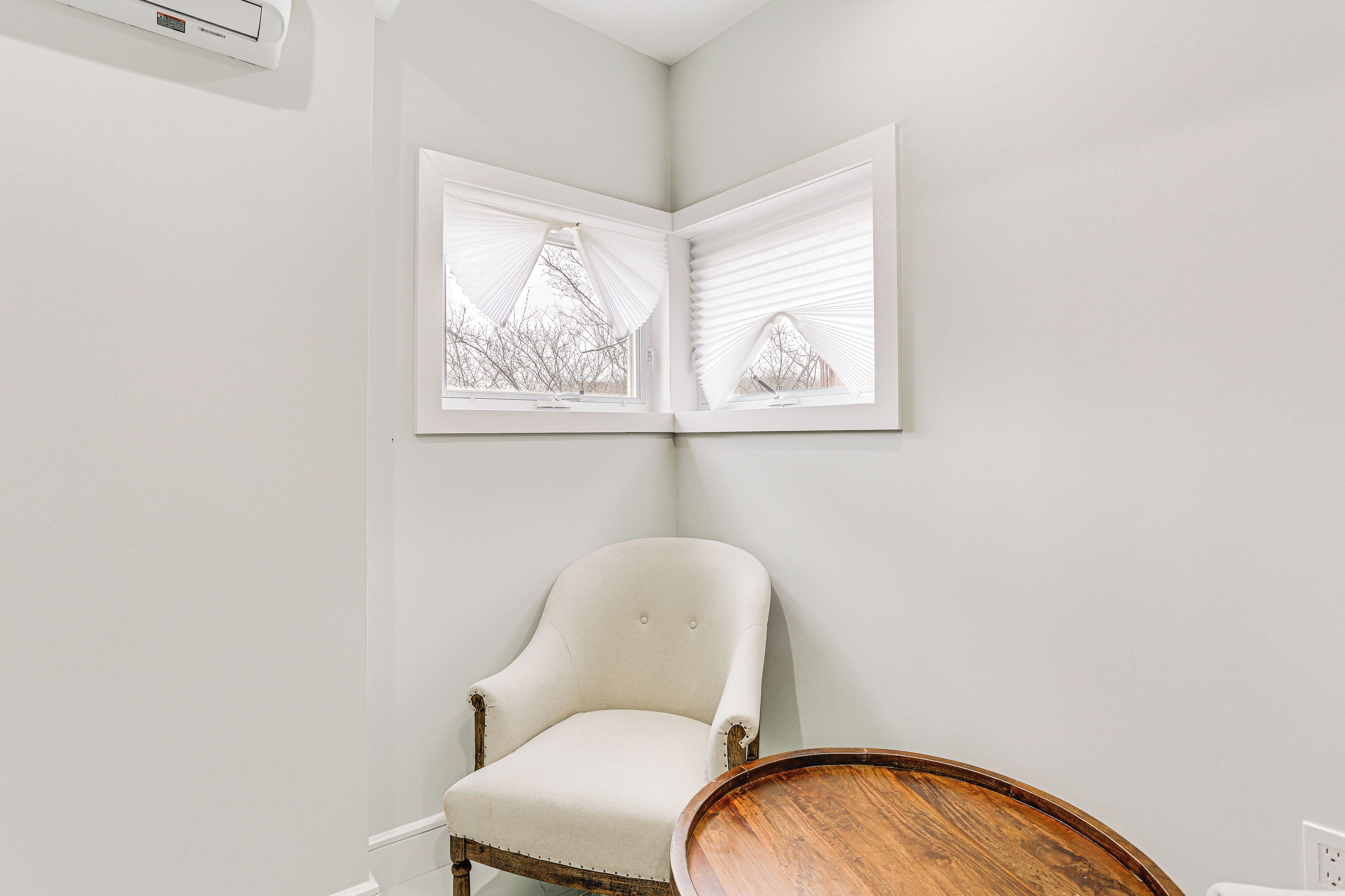 A corner room with a white chair, a wooden table, and a window with blinds.