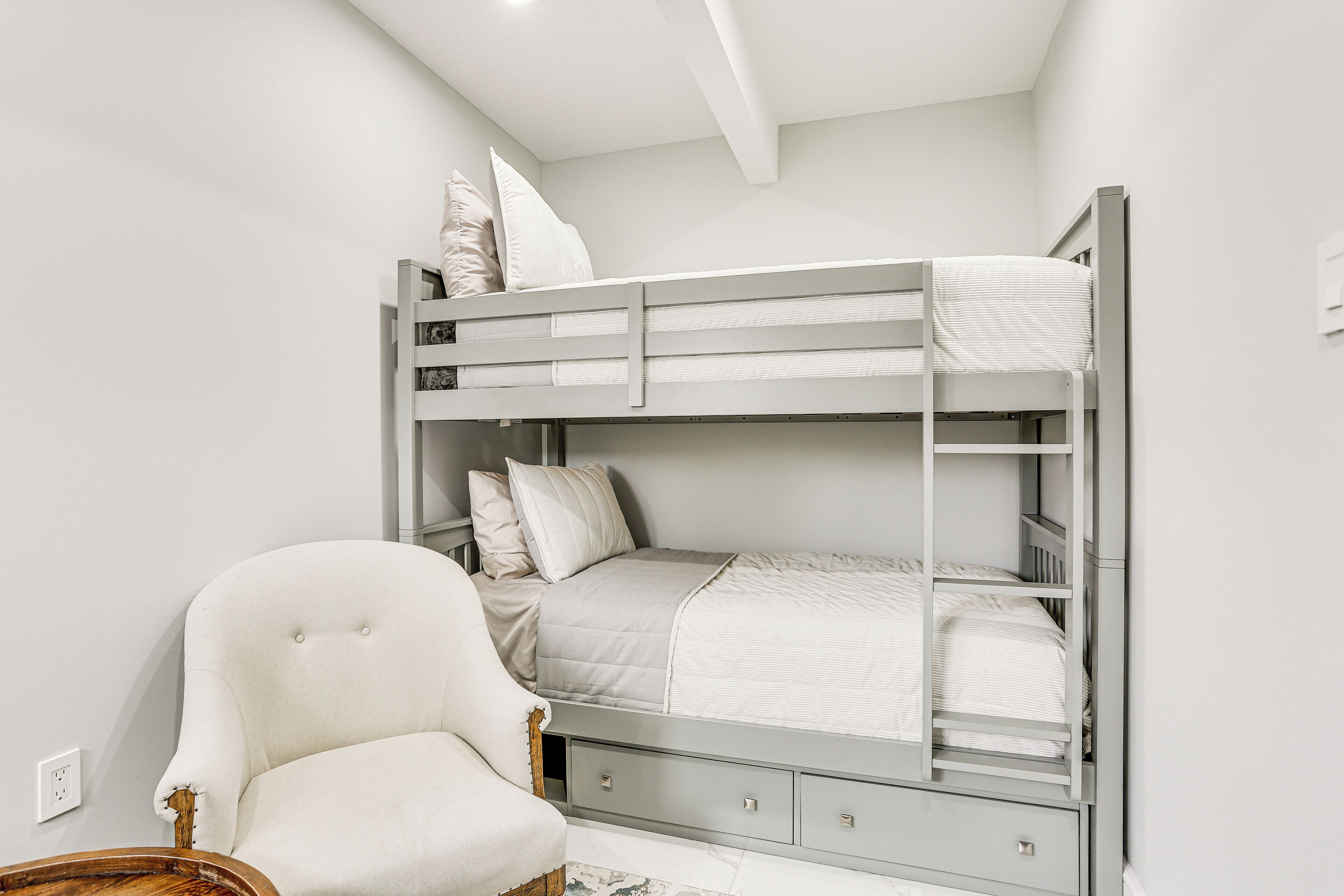 Un lit superposé avec une chaise et une petite table dans une pièce aux murs blancs et au plafond en pente.