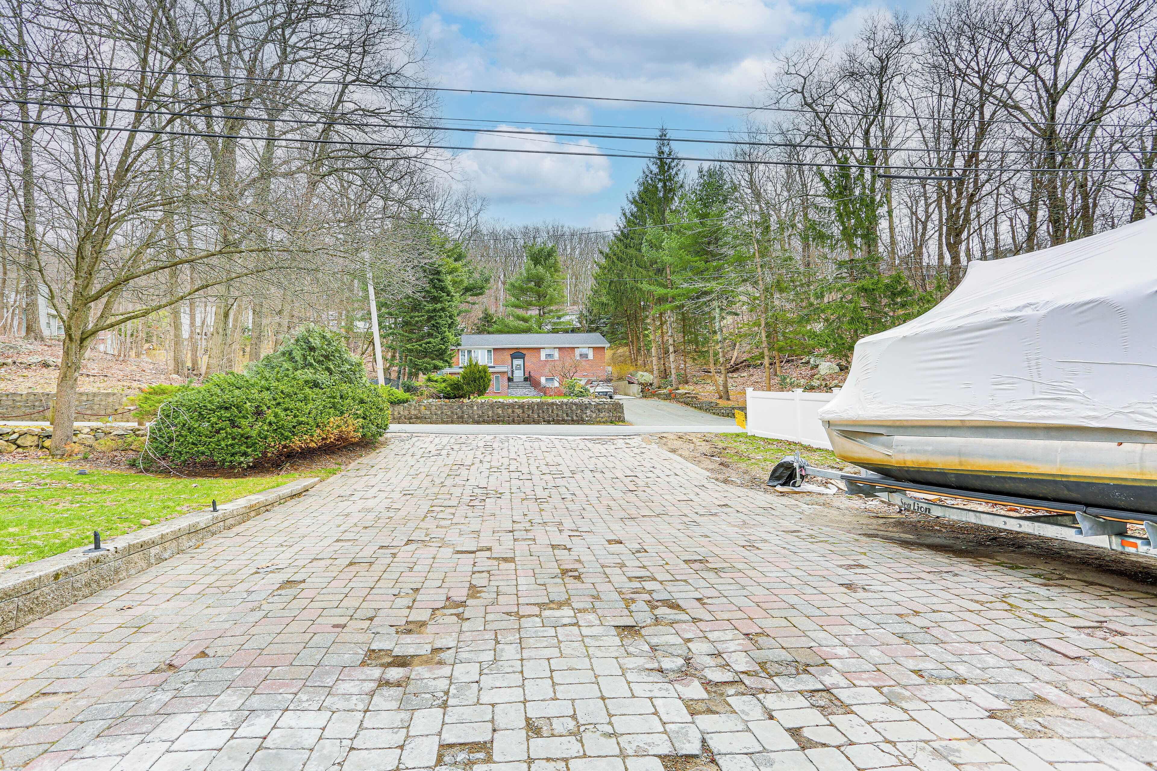 A paved driveway leading to a house with a boat covered in a white tarp.
