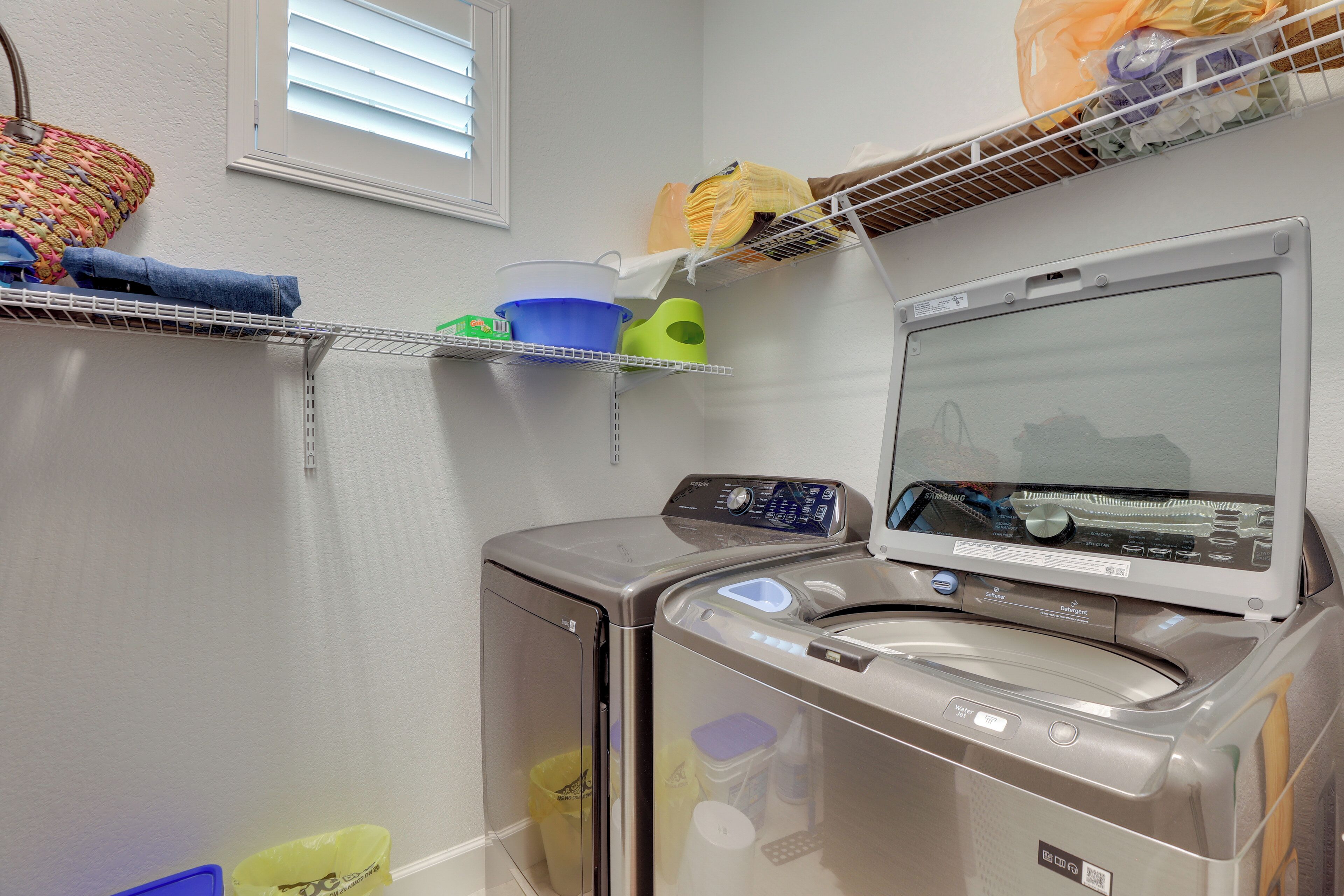 A laundry area with a front-loading washer and dryer, shelves with folded clothes, and laundry baskets.