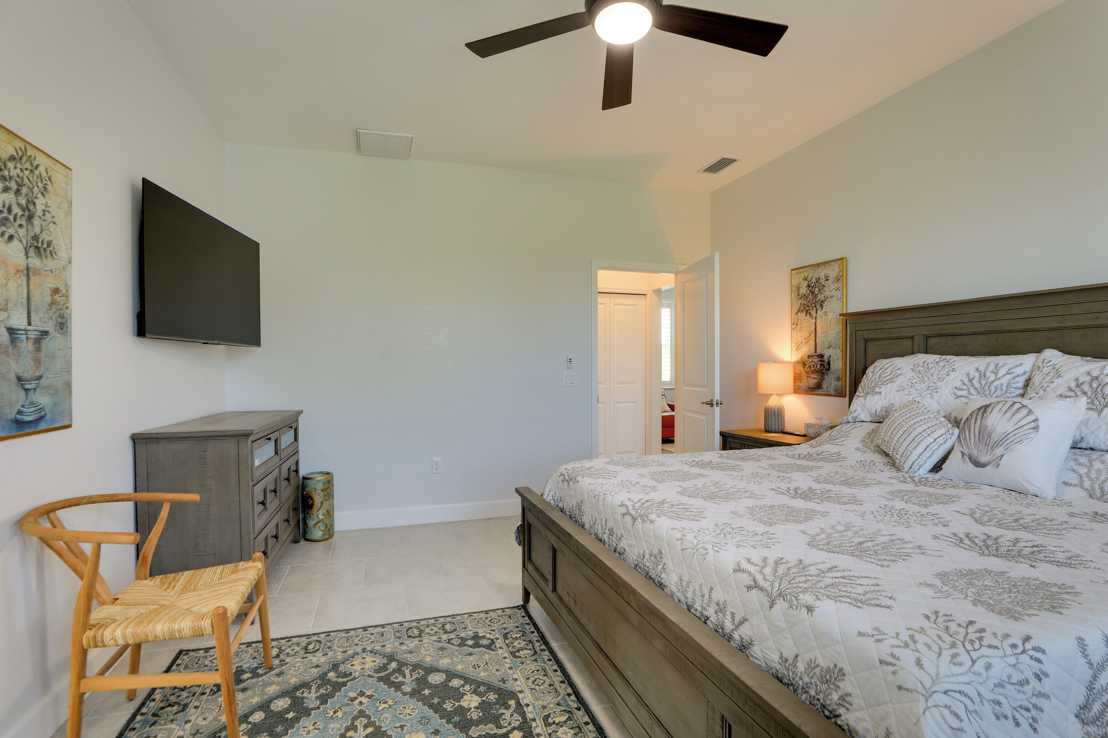 A bedroom with a bed, a desk, a chair, a ceiling fan, and artwork on the walls.