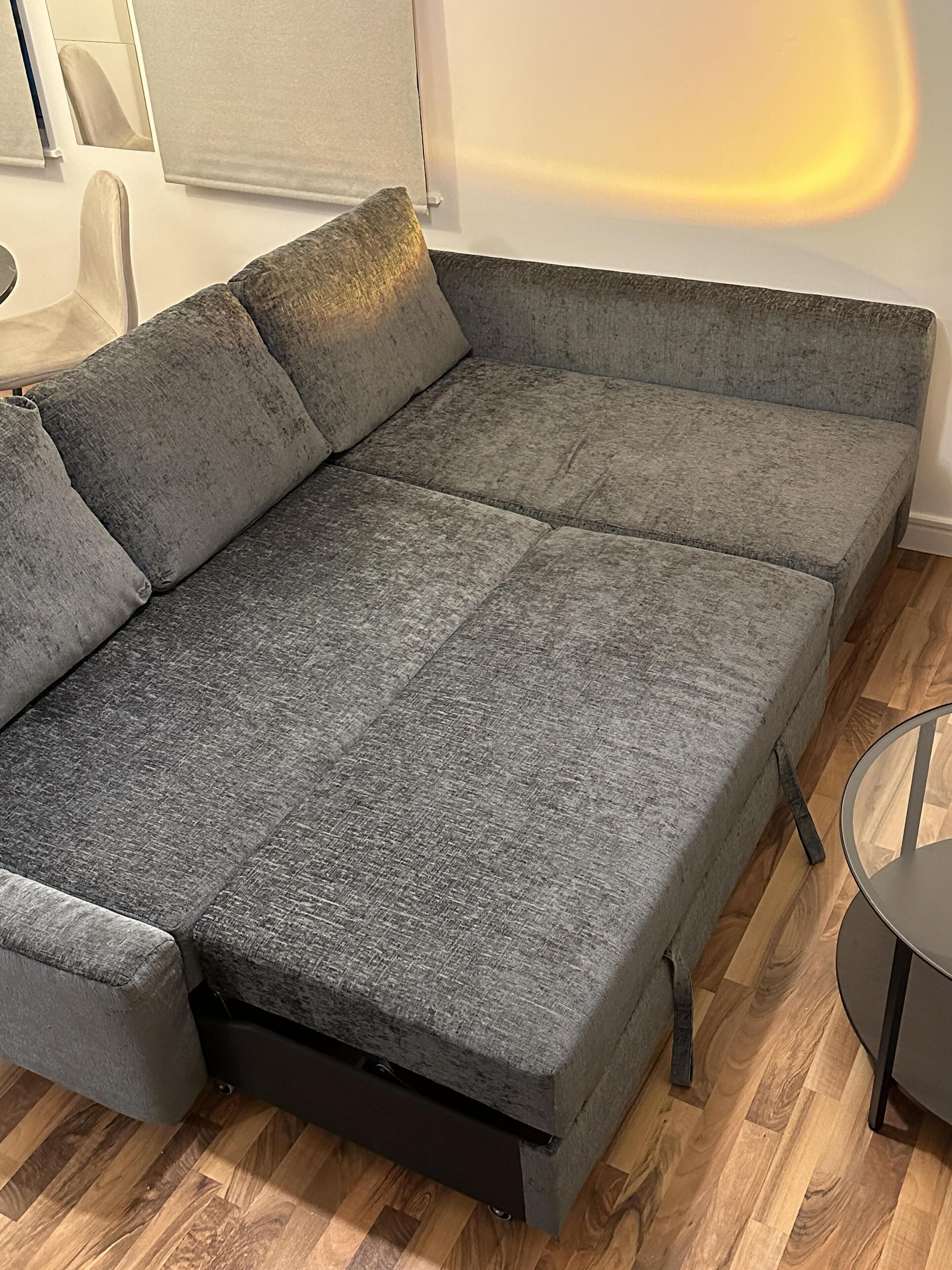 Un divano angolare grigio con letto estraibile, su un pavimento in legno.