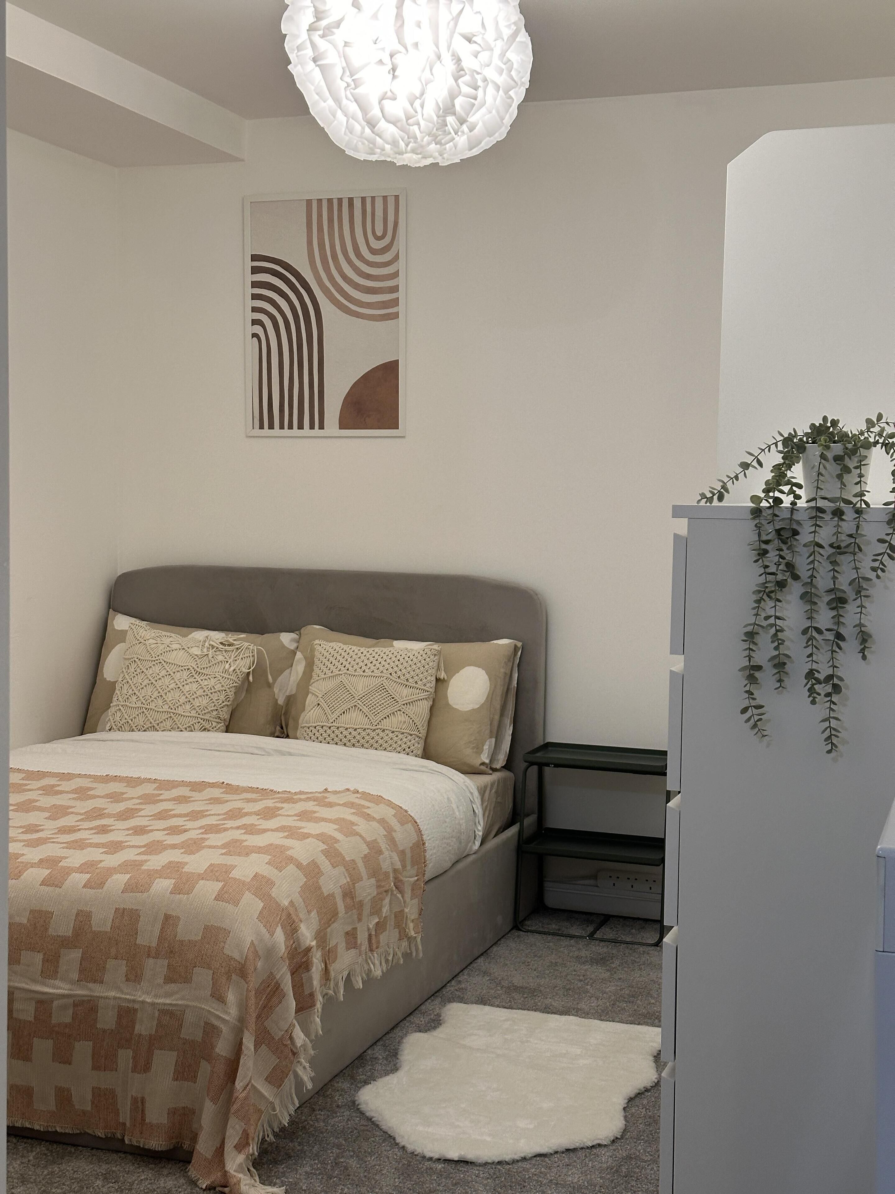 A bedroom with a bed, a bedside table, a nightstand, a wall-mounted plant, and a ceiling light fixture.