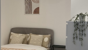 Une chambre à coucher comprenant un lit, une table de chevet, une commode, une plante fixée au mur et un luminaire au plafond.