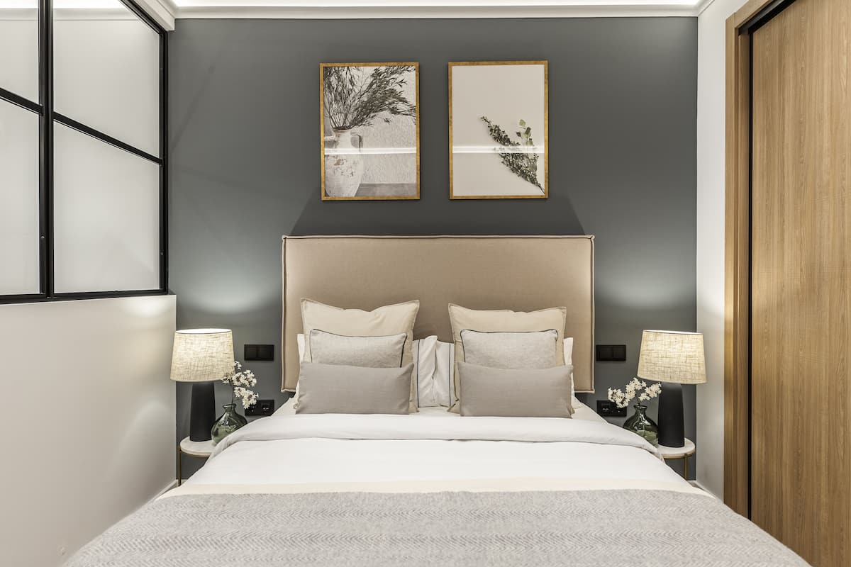 A modern bedroom with a large bed, two bedside tables with lamps, and two framed artworks on the wall.