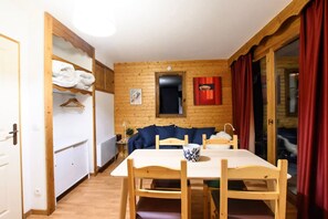 Une pièce chaleureuse avec un mur en bois, une table à manger avec des chaises, un canapé et un rideau rouge.