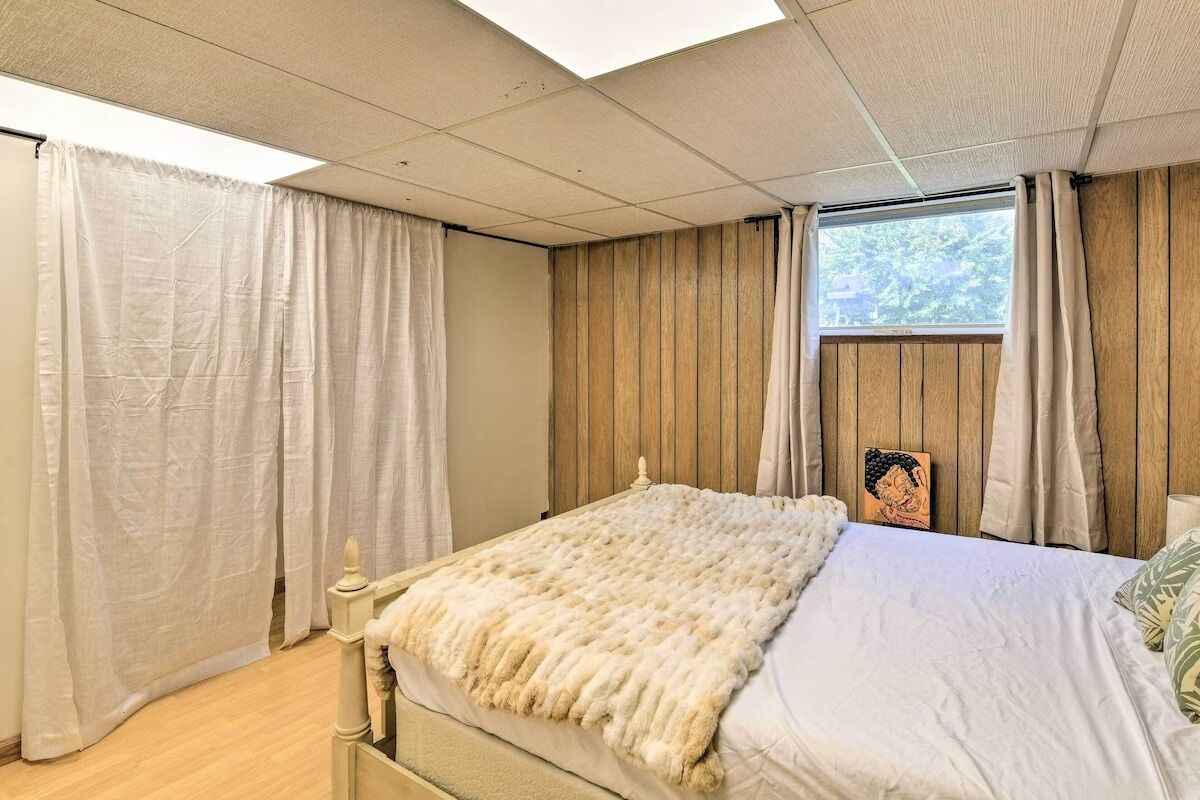 A bedroom with a bed, curtains, a wooden headboard, and a window with a view of trees.