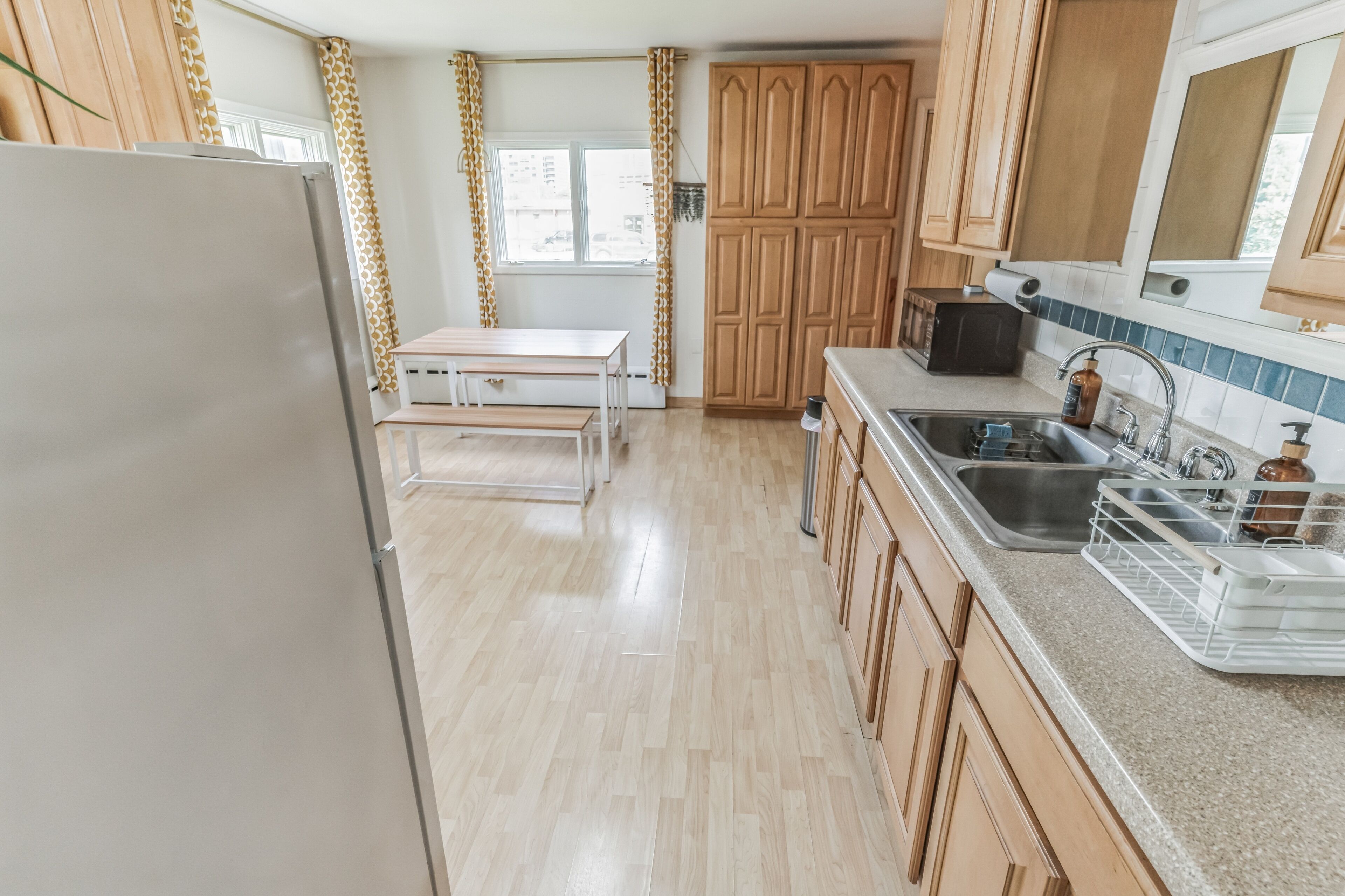 Una cocina con armarios de madera, un refrigerador de acero inoxidable, una mesa de madera y un lavamanos con dispensador de jabón.