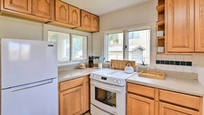 Une cuisine avec des meubles de rangement en bois, un réfrigérateur blanc, une cuisinière et une fenêtre avec des stores.