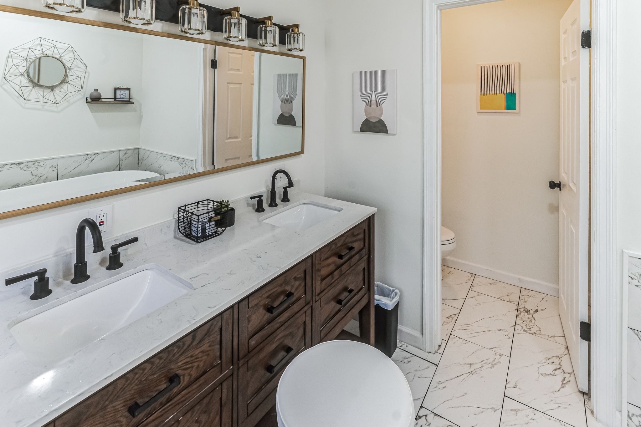 A bathroom with a large mirror, two sinks, wooden cabinets, and a toilet.