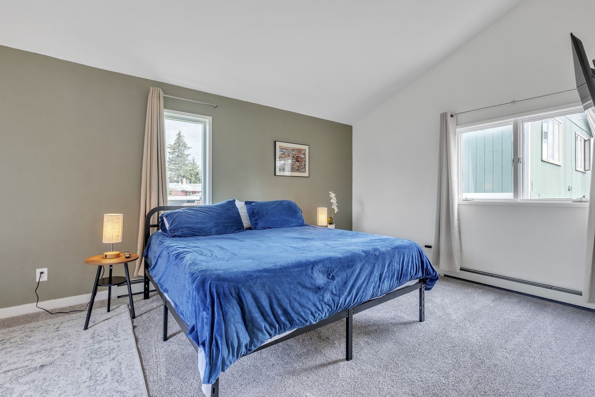 A bedroom with a bed, a nightstand, a lamp, a window, and a wall-mounted TV.