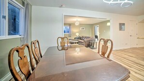 Uma sala de jantar com mesa e cadeiras de madeira, um sofá e uma luminária moderna.