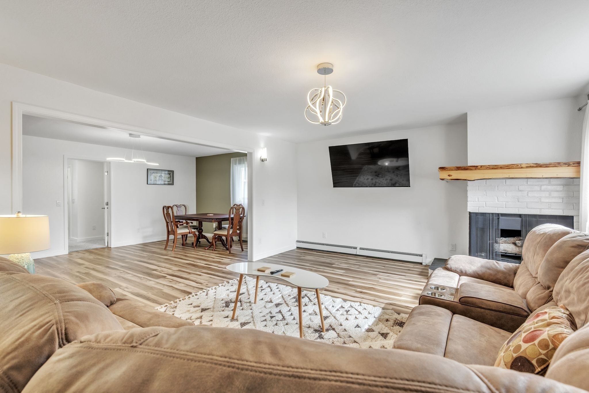Uma sala de estar moderna com piso de madeira, sofás bege, uma mesa de centro e uma lareira.