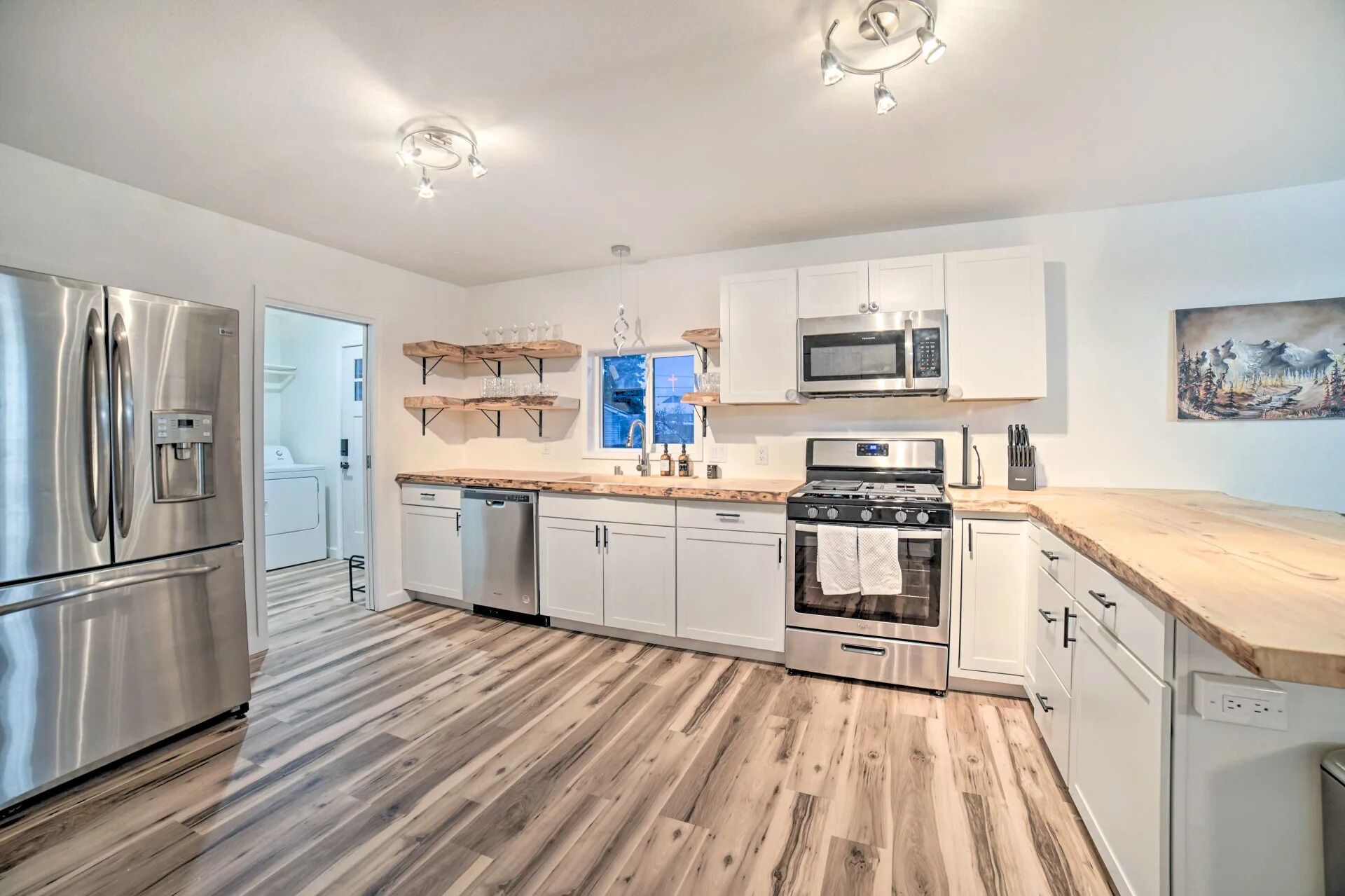 A modern kitchen with stainless steel appliances, wooden flooring, and white cabinetry.