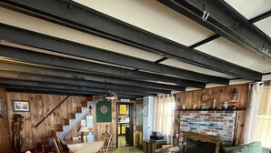 Ein geräumiges Wohnzimmer mit hoher Decke, freiliegenden Balken, einem Kamin und einer Treppe, die zu einer oberen Ebene führt.