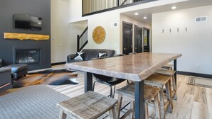 A spacious living area with a large wooden dining table, black leather sofa, and a fireplace. - Great Access just Off Hwy, Hot Tub, Open Plan w/ Parking! Close to Town! (Lead)