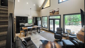 A modern kitchen with a dining area, a living room with a fireplace, and large windows offering a view of the outdoors. - Great Access just Off Hwy, Hot Tub, Open Plan w/ Parking! Close to Town! (Lead)