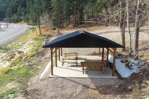 A wooden pavilion with picnic tables and benches, surrounded by a gravel area and trees. - Great Access just Off Hwy, Hot Tub, Open Plan w/ Parking! Close to Town! (Lead)