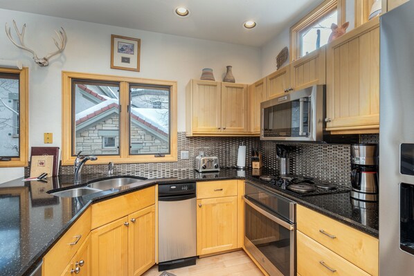 A modern kitchen with wooden cabinets, stainless steel appliances, and a black countertop.