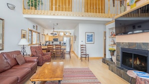 A spacious living area with a high ceiling, a fireplace, a dining area, and a kitchen in the background. - Mountain View Haven Townhouse by Alpine Lodging Telluride (Telluride)
