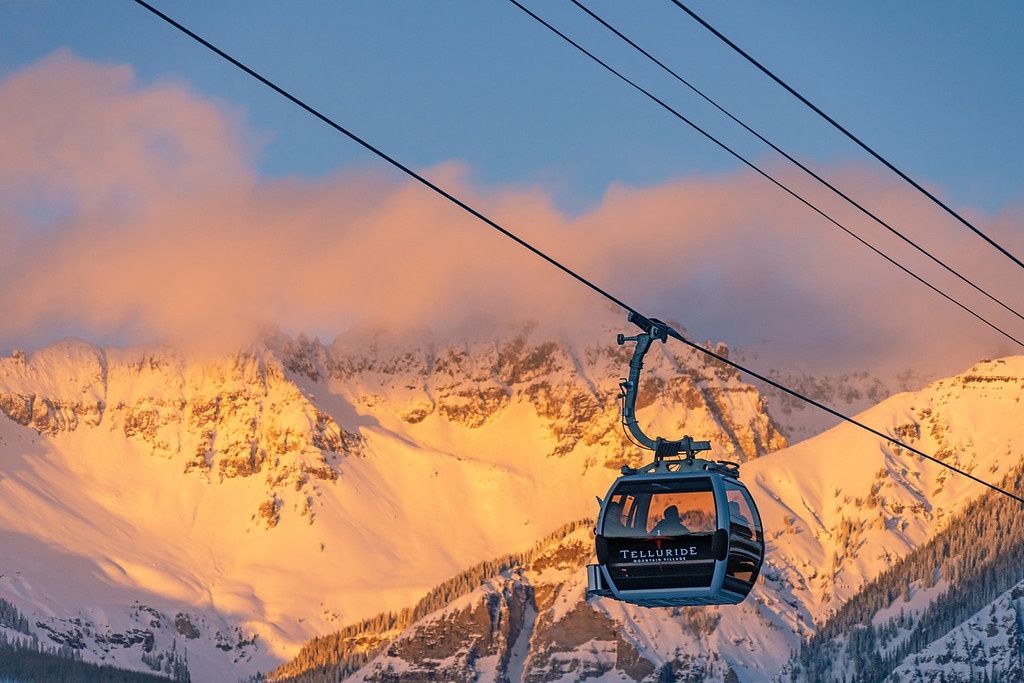 A cable car with 'TELLURIDE' written on it, suspended by cables against a mountainous backdrop.