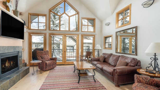A spacious living room with a fireplace, large windows, and a cozy seating area. - Mountain View Haven Townhouse by Alpine Lodging Telluride (Telluride)
