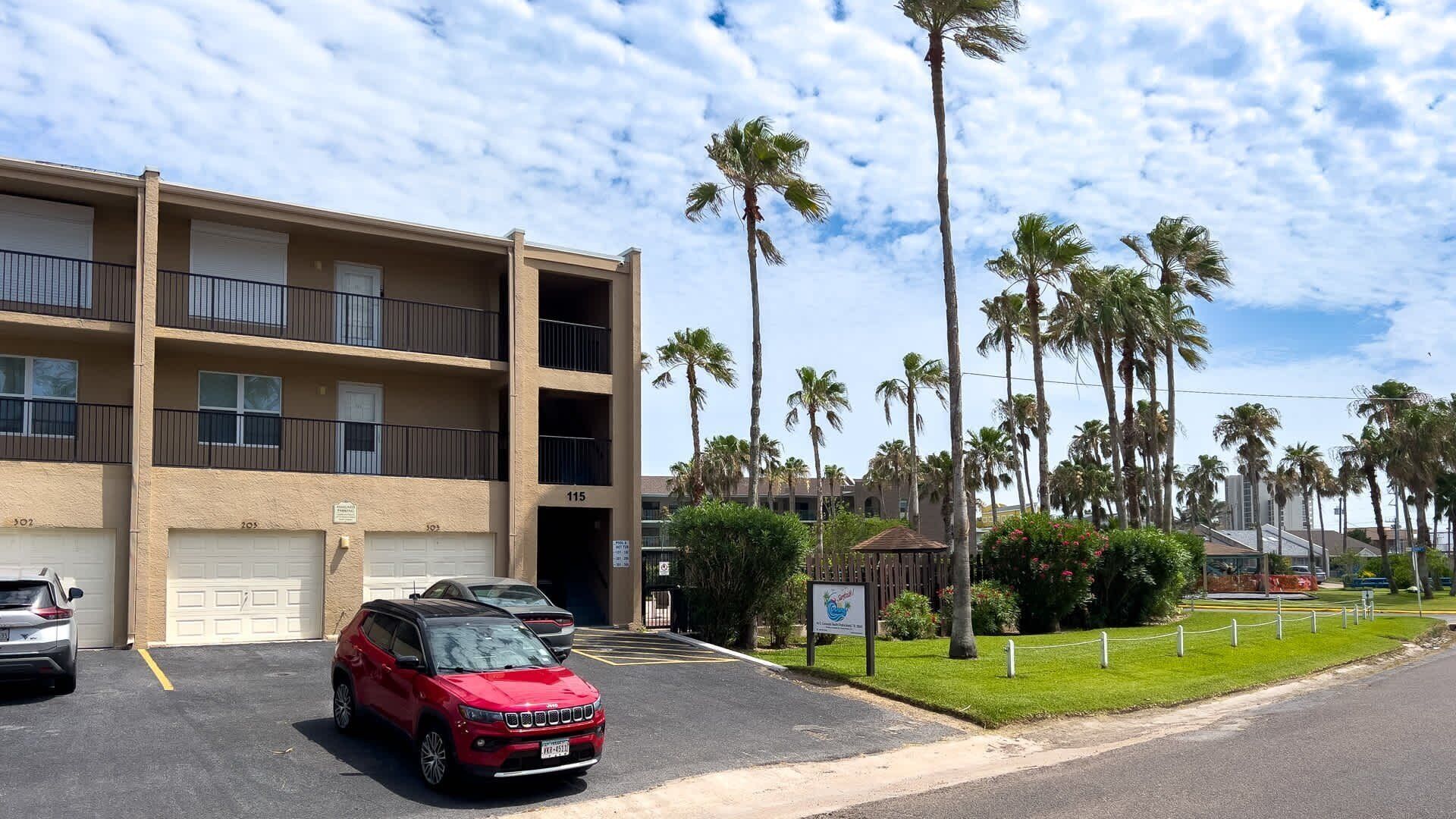 A multi-story building with parking spaces and a red SUV parked in front.