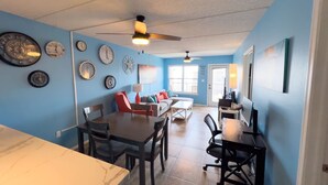 A dining area with a table and chairs, a sofa, and a ceiling fan. - Surfside I #304 2 Bedroom Condo by RedAwning (South Padre Island)
