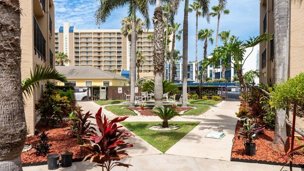 A hotel courtyard with palm trees, a fountain, and a pool area. - Surfside I #304 2 Bedroom Condo by RedAwning (South Padre Island)