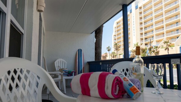A balcony with white chairs, a striped towel, and a bottle of alcohol. - Surfside Ii #109 2 Bedroom Home by RedAwning (South Padre Island)