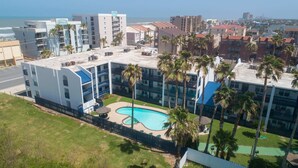A hotel with a rooftop pool, surrounded by palm trees and a view of the ocean. - Surfside Ii #109 2 Bedroom Home by RedAwning (South Padre Island)