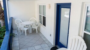 A small patio with a white table and chairs, a blue door, and a window with blinds. - Surfside Ii #109 2 Bedroom Home by RedAwning (South Padre Island)