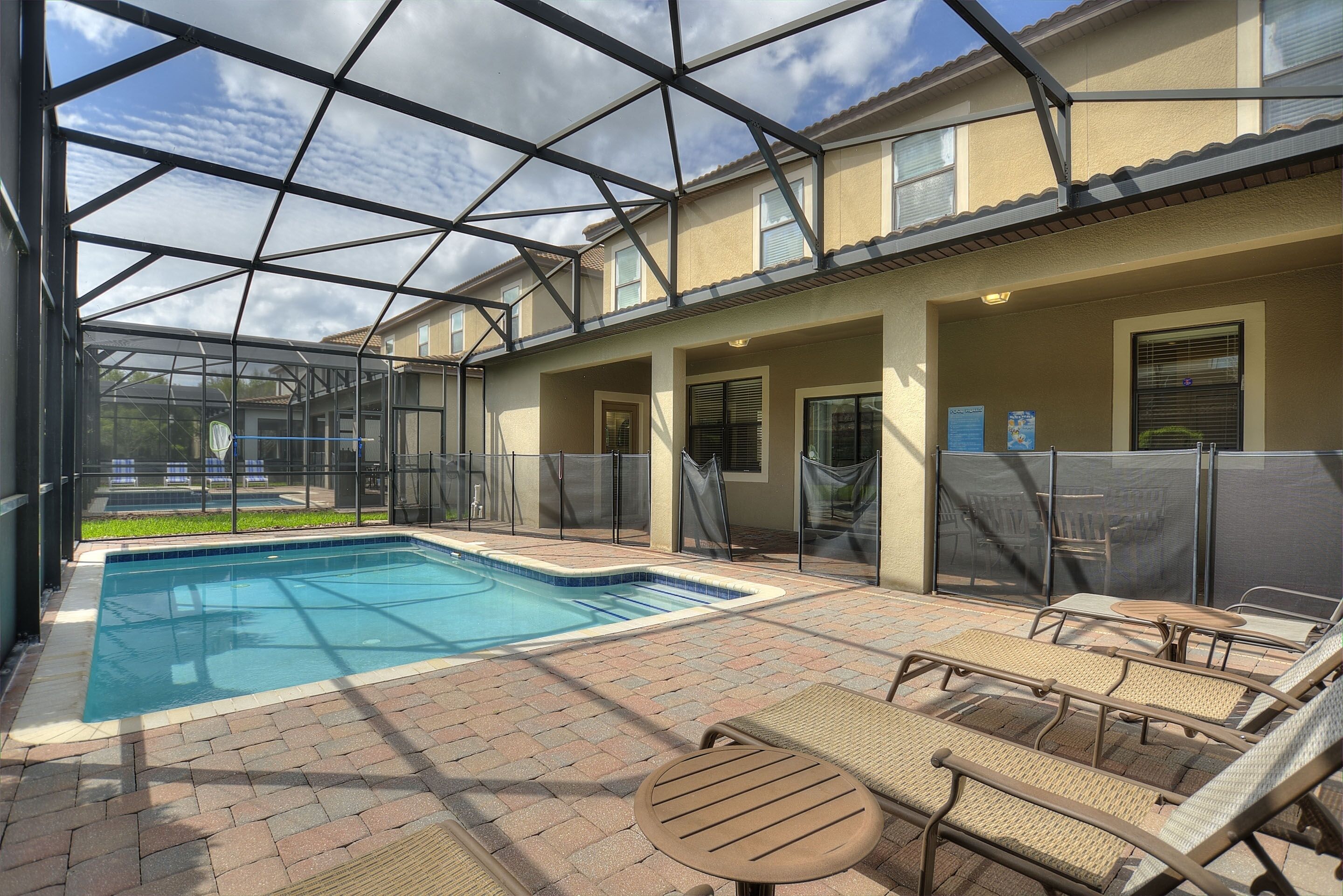 A pool area with a glass enclosure, lounge chairs, and a brick patio.
