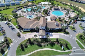 An aerial view of a resort with multiple swimming pools, a central building with a tiled roof, and surrounding landscaped areas. - Southern Sun At Championsgate Resort By Shine Villas 446 6 Bedroom Villa (Davenport)