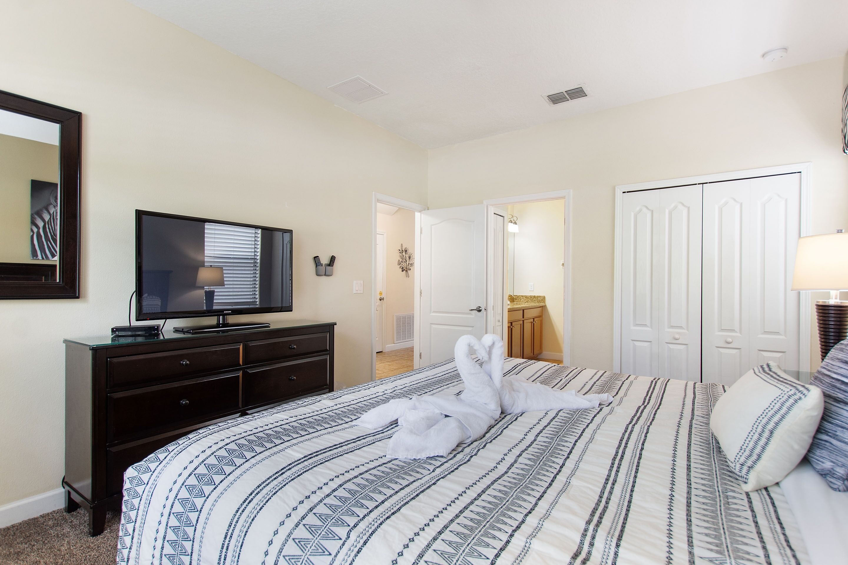 A hotel room with a bed, a TV, a dresser, and a door leading to another room.