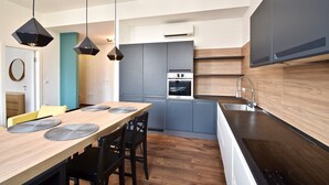 A modern kitchen with a wooden dining table, black pendant lights, and built-in appliances. - Modern apartment with 2 bedrooms near Arena (Pula)