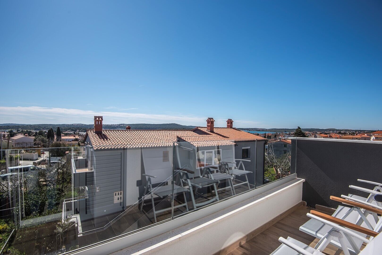 A rooftop terrace with a clear view of the cityscape, a small building with a tiled roof, and a glass railing.