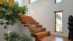 Un escalier moderne avec des marches en bois et une rampe en verre, menant à un palier offrant une vue sur l’extérieur.