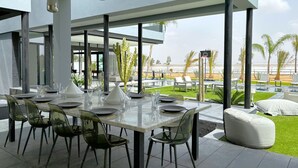 Un espace extérieur aménagé pour prendre les repas, offrant une vue dégagée sur la plage et les palmiers.