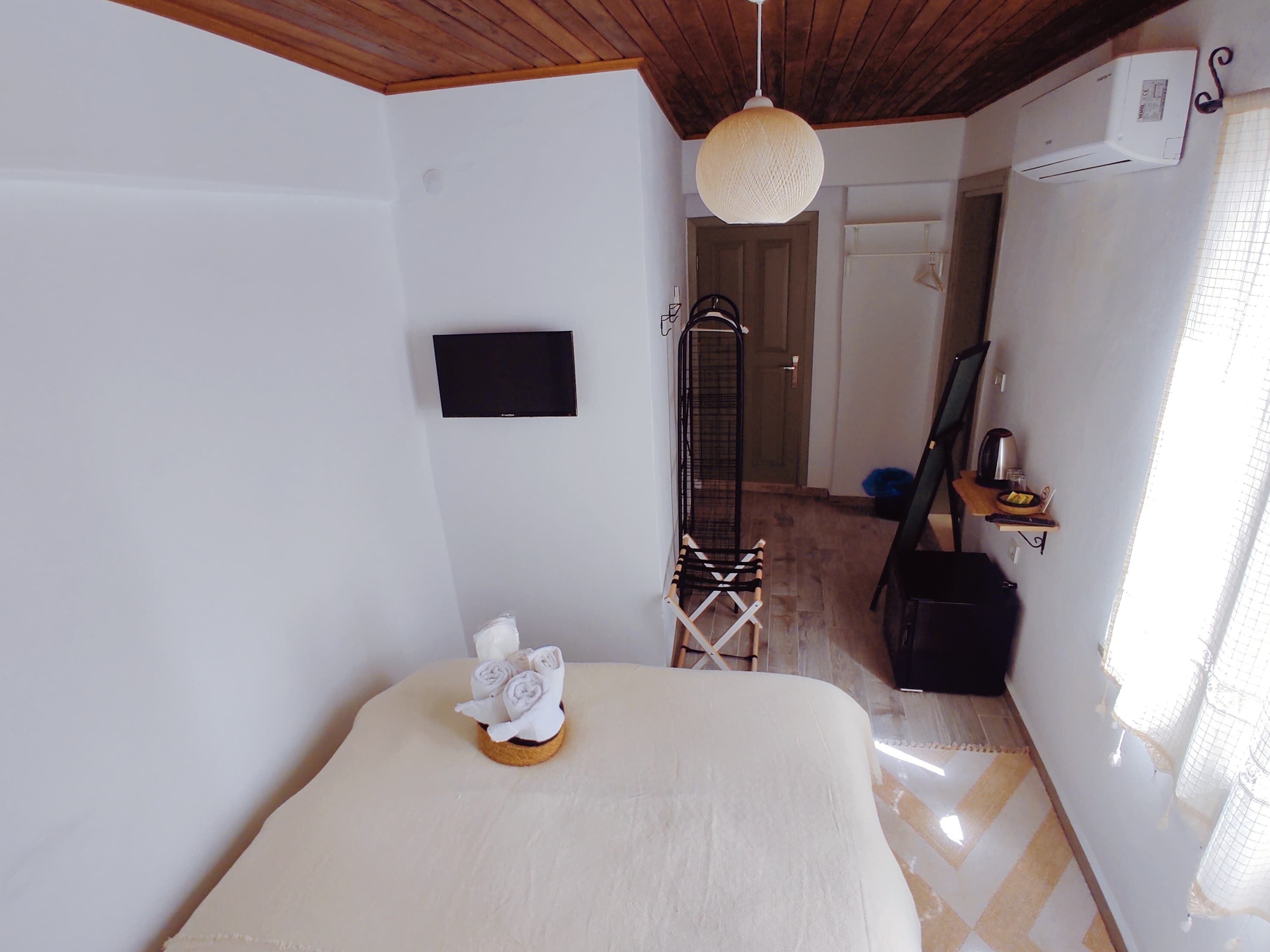 A hotel room with a bed, a TV mounted on the wall, a hanging light fixture, and a door leading to another room.